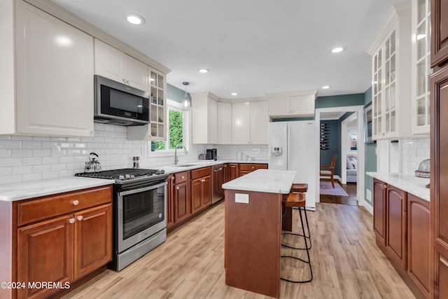 kitchen featuring light wood finished floors, a kitchen island, a breakfast bar, stainless steel appliances, and a sink