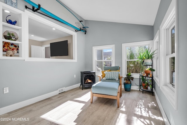 sitting room featuring visible vents, lofted ceiling, wood finished floors, baseboards, and a wood stove