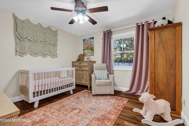 bedroom with ceiling fan, baseboards, a crib, and wood finished floors