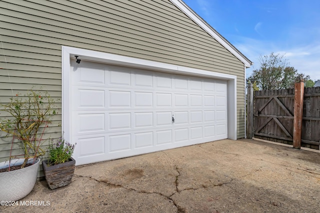 garage featuring concrete driveway, fence, and a gate