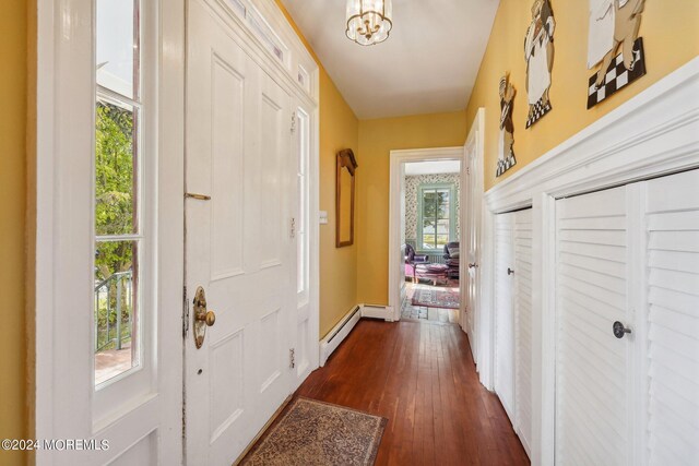 doorway to outside with baseboards, dark wood-style floors, a baseboard heating unit, and an inviting chandelier