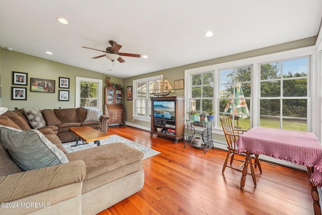 living area with light wood-style floors, plenty of natural light, baseboard heating, and a ceiling fan