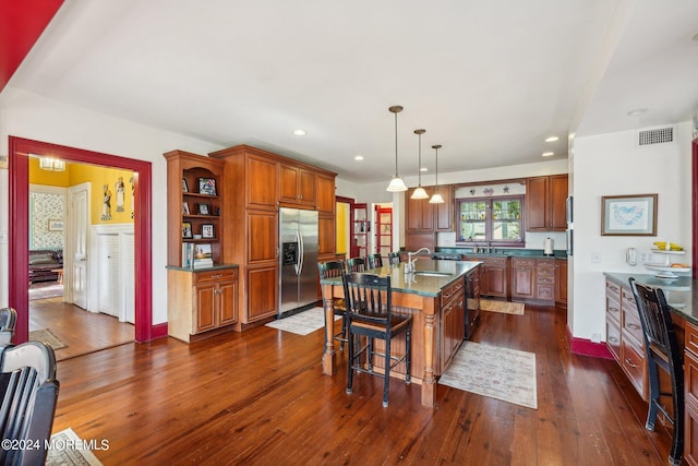 kitchen with stainless steel fridge, a sink, dark wood-style flooring, brown cabinets, and a breakfast bar area
