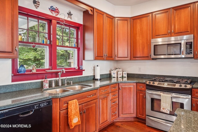 kitchen with dark stone countertops, appliances with stainless steel finishes, dark wood-style flooring, a sink, and brown cabinets