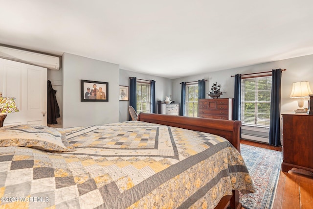 bedroom with an AC wall unit, multiple windows, hardwood / wood-style floors, and baseboard heating