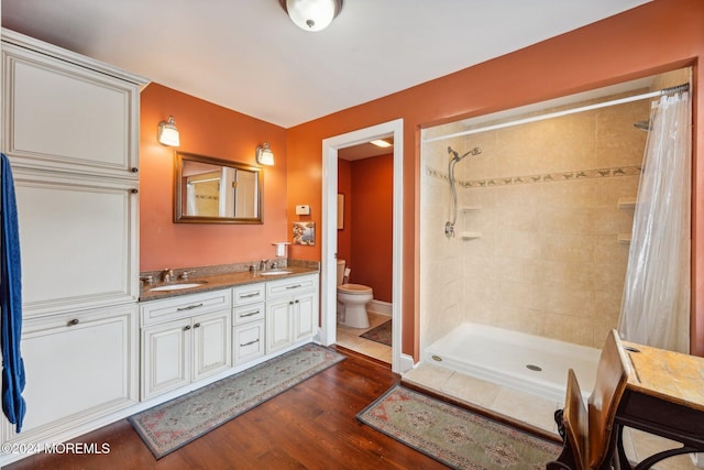 full bath with a tile shower, wood finished floors, a sink, and toilet