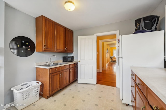 kitchen with black microwave, light countertops, freestanding refrigerator, brown cabinetry, and a sink