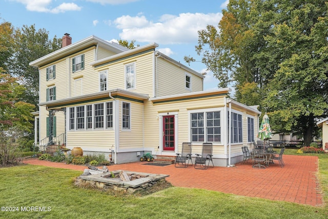 rear view of house featuring entry steps, a chimney, a lawn, and a patio area