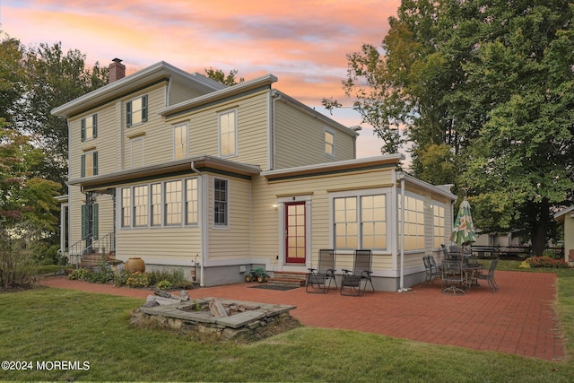 back of house at dusk featuring a patio area, entry steps, a chimney, and a lawn