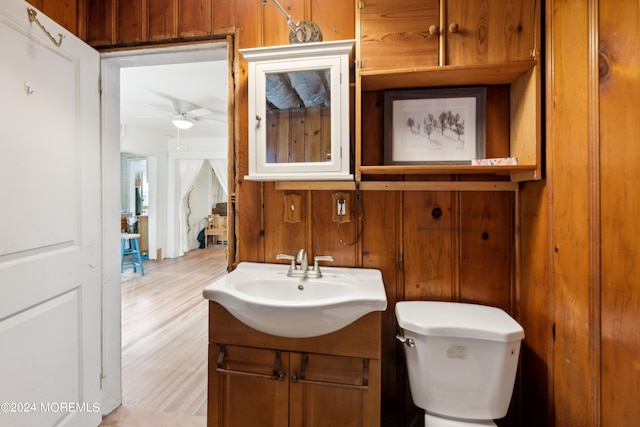 bathroom with wood walls, ceiling fan, vanity, and toilet