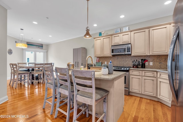 kitchen with appliances with stainless steel finishes, hanging light fixtures, an island with sink, light stone counters, and light hardwood / wood-style flooring