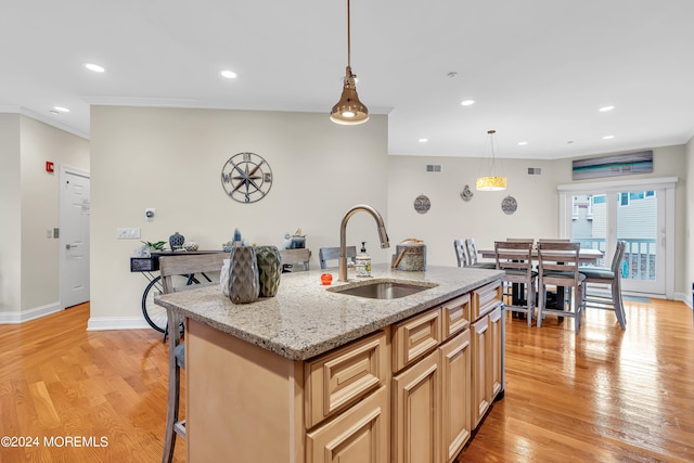 kitchen with a kitchen island with sink, sink, light hardwood / wood-style flooring, and light stone counters