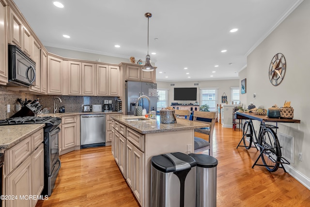 kitchen with appliances with stainless steel finishes, light stone counters, an island with sink, light wood-type flooring, and decorative light fixtures