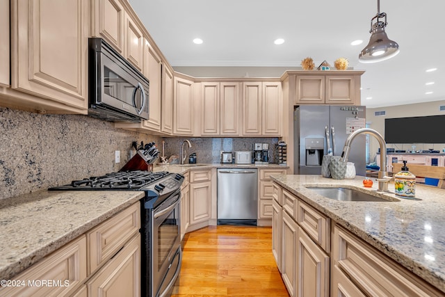 kitchen featuring pendant lighting, sink, light hardwood / wood-style flooring, stainless steel appliances, and light stone countertops