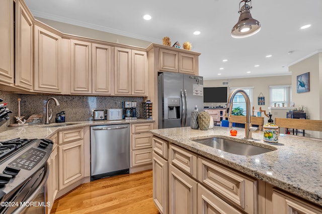 kitchen with light wood-type flooring, sink, stainless steel appliances, decorative light fixtures, and ornamental molding