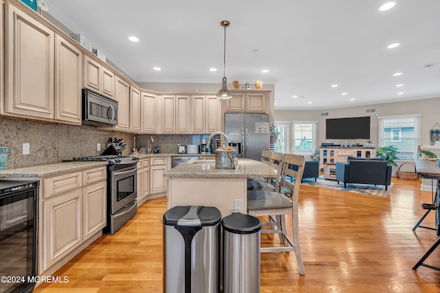 kitchen featuring an island with sink, hanging light fixtures, stainless steel appliances, light stone countertops, and light hardwood / wood-style floors