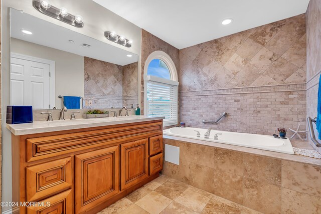 bathroom with tile walls, a relaxing tiled tub, and vanity