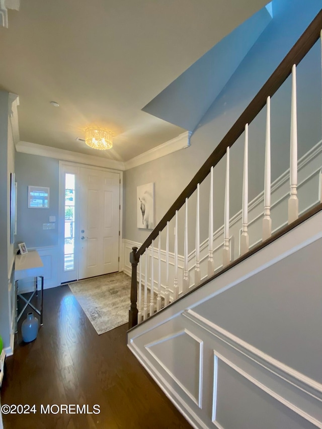 entryway with ornamental molding, an inviting chandelier, and dark wood-type flooring