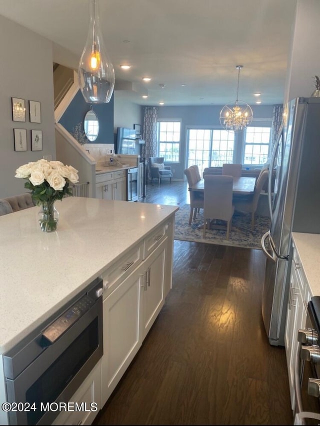 kitchen featuring appliances with stainless steel finishes, hanging light fixtures, white cabinetry, light stone counters, and dark hardwood / wood-style flooring