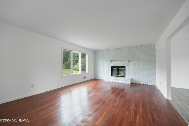 unfurnished living room with a brick fireplace, brick wall, and dark wood-type flooring