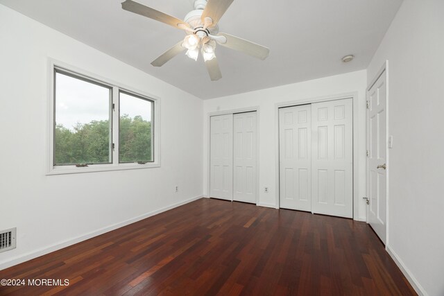 unfurnished bedroom with two closets, ceiling fan, and dark hardwood / wood-style flooring