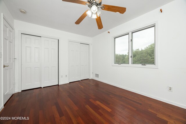 unfurnished bedroom featuring multiple closets, ceiling fan, and dark wood-type flooring