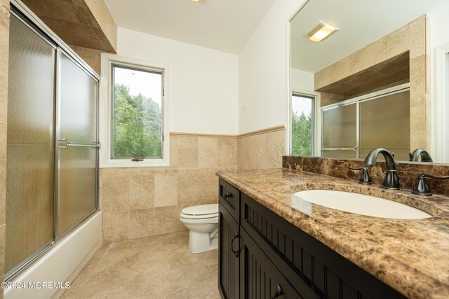 full bathroom with tile walls, vanity, shower / bath combination with glass door, toilet, and tile patterned floors