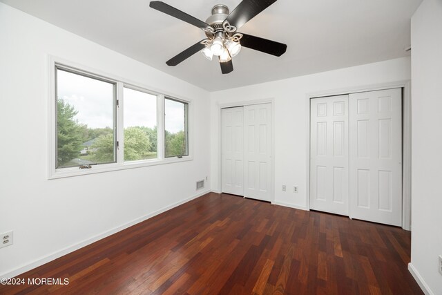 unfurnished bedroom with multiple closets, ceiling fan, and dark hardwood / wood-style floors