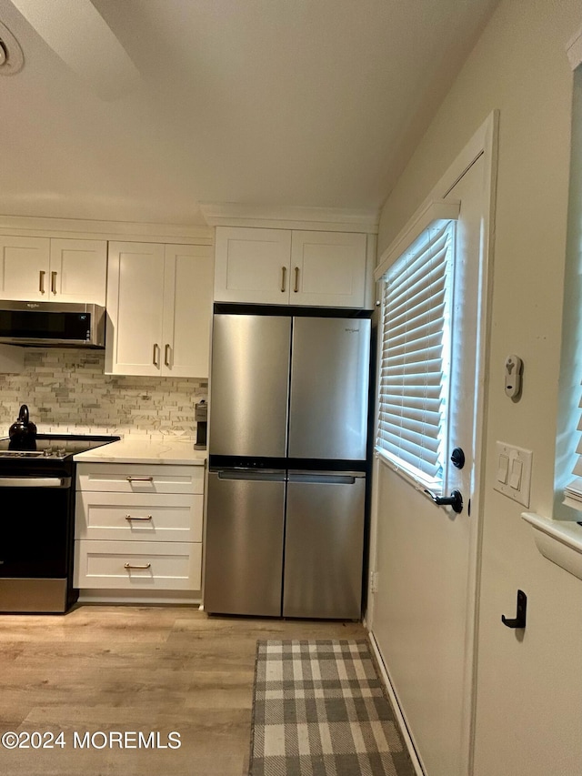 kitchen featuring white cabinetry, exhaust hood, appliances with stainless steel finishes, light wood-type flooring, and decorative backsplash