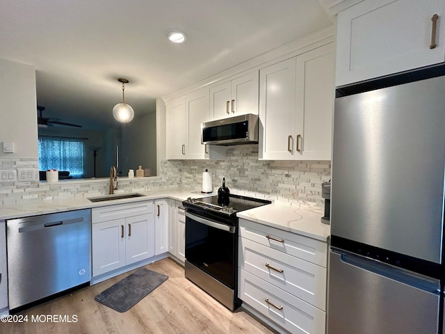 kitchen with light wood-type flooring, sink, white cabinetry, stainless steel appliances, and decorative light fixtures