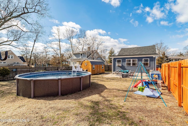 view of yard featuring an outbuilding, a playground, a shed, a fenced backyard, and a fenced in pool