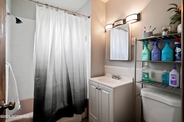 bathroom with toilet, tile walls, wainscoting, vanity, and shower / bath combo with shower curtain