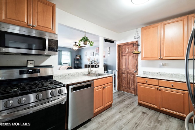 kitchen with light wood-style flooring, stainless steel appliances, a sink, light stone counters, and ceiling fan