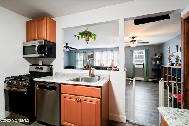 kitchen with dark wood-style floors, appliances with stainless steel finishes, open floor plan, a sink, and brown cabinetry