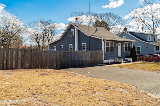 view of front of home featuring fence, a shingled roof, and a chimney