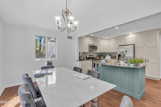 dining space with an inviting chandelier, light wood-type flooring, and vaulted ceiling