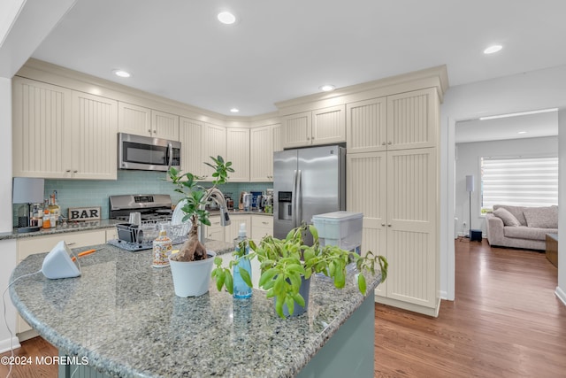 kitchen featuring tasteful backsplash, a center island with sink, appliances with stainless steel finishes, light stone countertops, and wood-type flooring