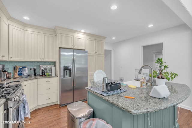 kitchen with a center island with sink, backsplash, light stone countertops, light hardwood / wood-style floors, and stainless steel appliances