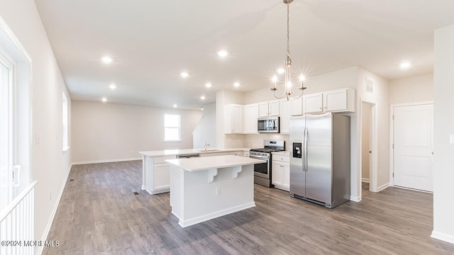 kitchen featuring appliances with stainless steel finishes, white cabinetry, wood-type flooring, decorative light fixtures, and sink