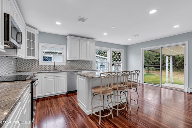 kitchen with light stone counters, a center island, dark wood-type flooring, white cabinetry, and stainless steel appliances