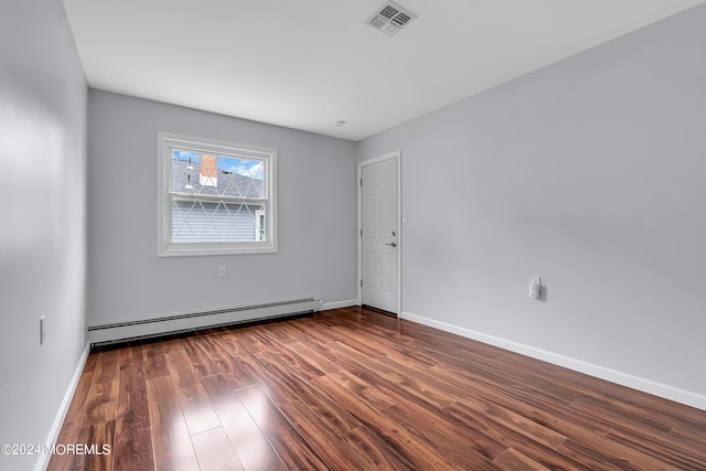 spare room featuring baseboard heating and dark hardwood / wood-style flooring