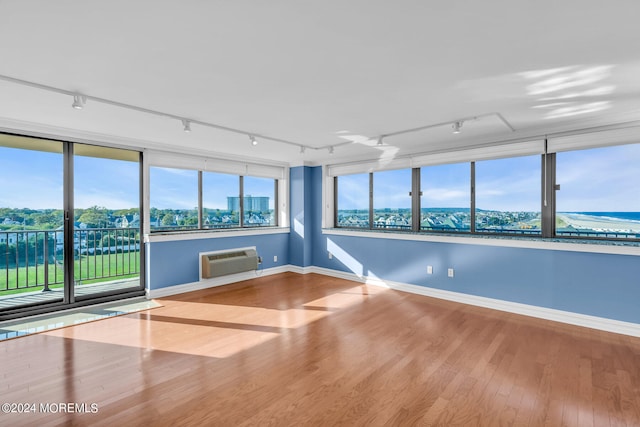 unfurnished room featuring an AC wall unit, hardwood / wood-style flooring, a healthy amount of sunlight, and rail lighting