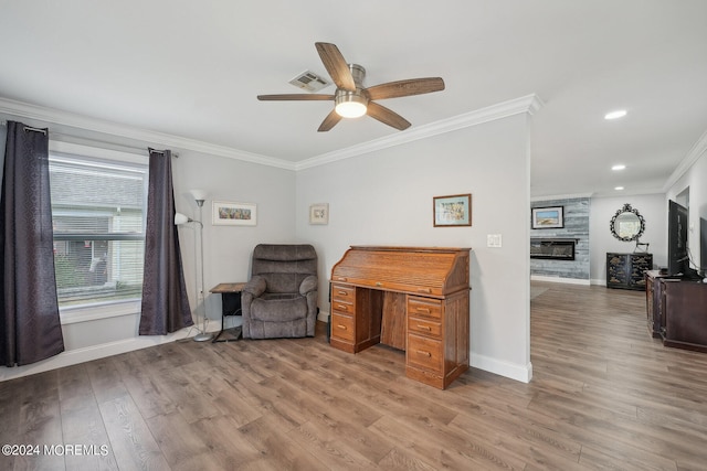 sitting room with ceiling fan, a stone fireplace, light hardwood / wood-style flooring, and crown molding