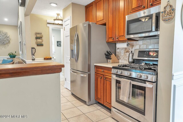 kitchen with decorative backsplash, stainless steel appliances, a textured ceiling, and light tile patterned floors