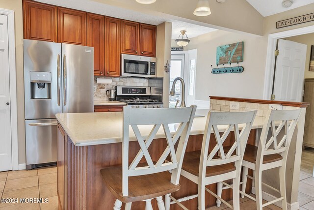 kitchen featuring appliances with stainless steel finishes, a kitchen island, light tile patterned floors, and tasteful backsplash