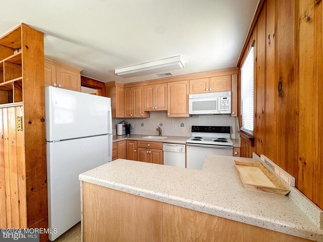 kitchen with sink, kitchen peninsula, decorative backsplash, white appliances, and light stone countertops