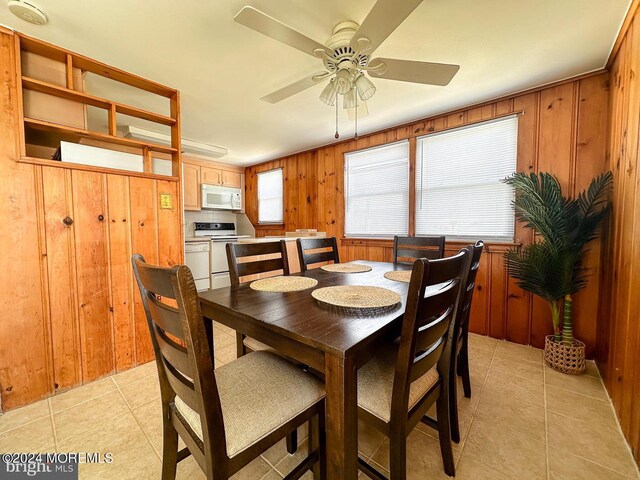 dining space with ceiling fan, wood walls, and light tile patterned floors