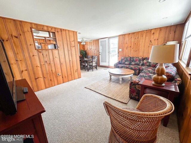 living room with a healthy amount of sunlight, wooden walls, and light colored carpet