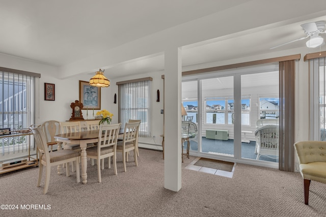 carpeted dining room featuring a water view, ceiling fan, baseboard heating, and a healthy amount of sunlight