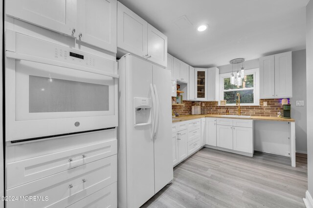 kitchen with white cabinets, hanging light fixtures, sink, white appliances, and light hardwood / wood-style floors